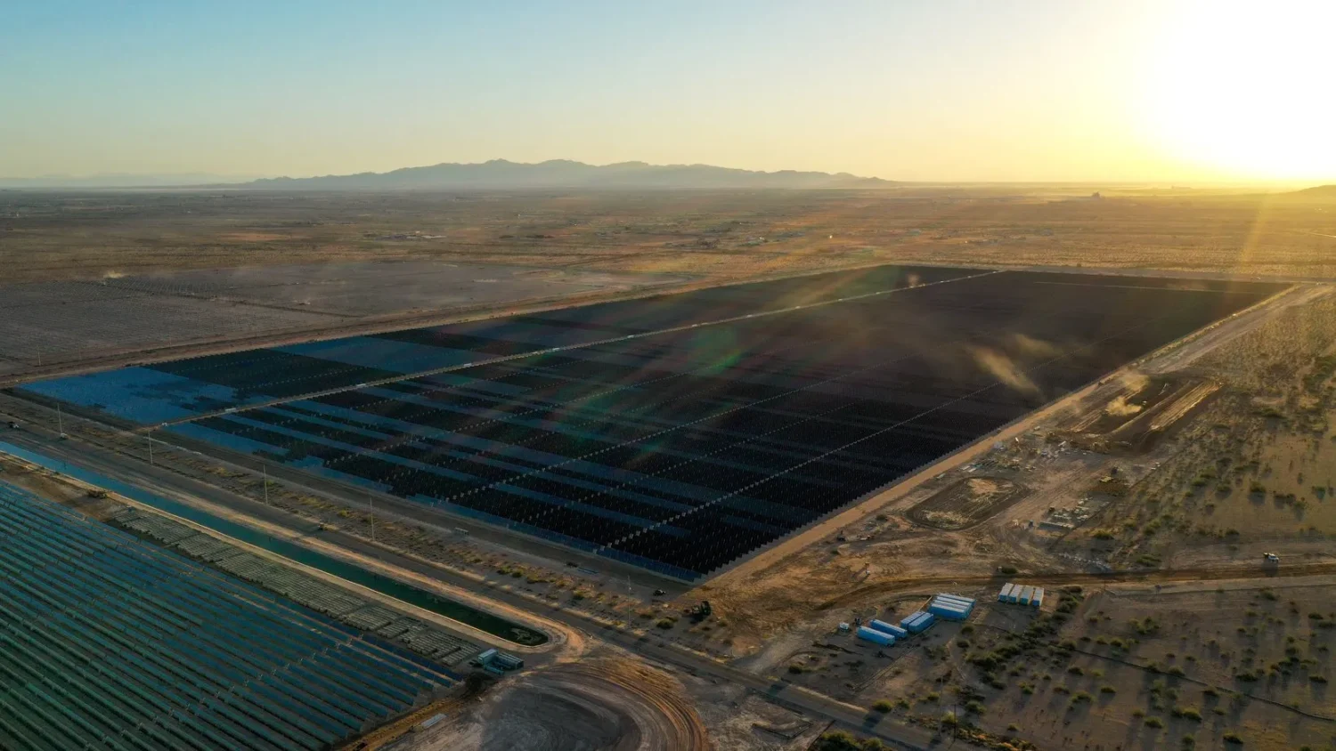 Aerial view of a vast agricultural field with rows of crops under the setting sun, highlighting intricate patterns and a dusty landscape.